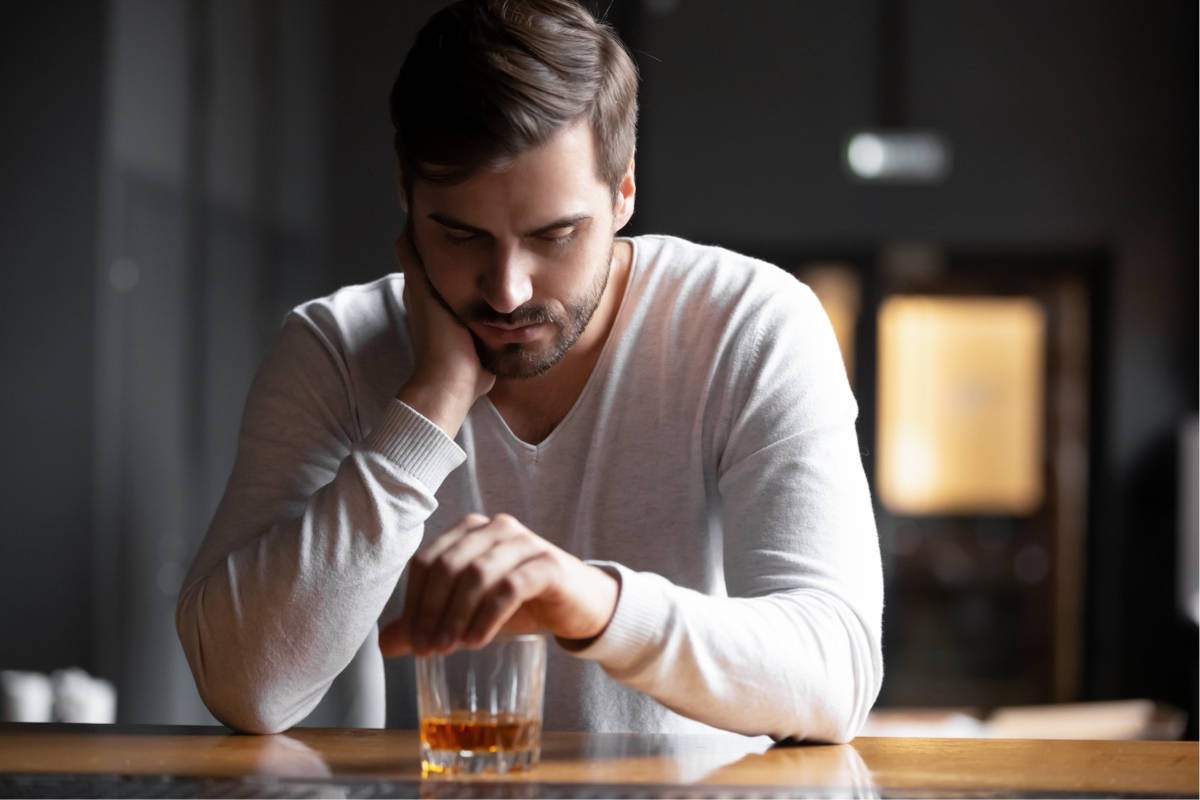 Ein Mann sitzt traurig am Tresen über einem Whiskyglas